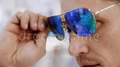 特写，英俊的年轻人在光学商店，光学零售店尝试蓝色太阳镜的肖像。 戴眼镜